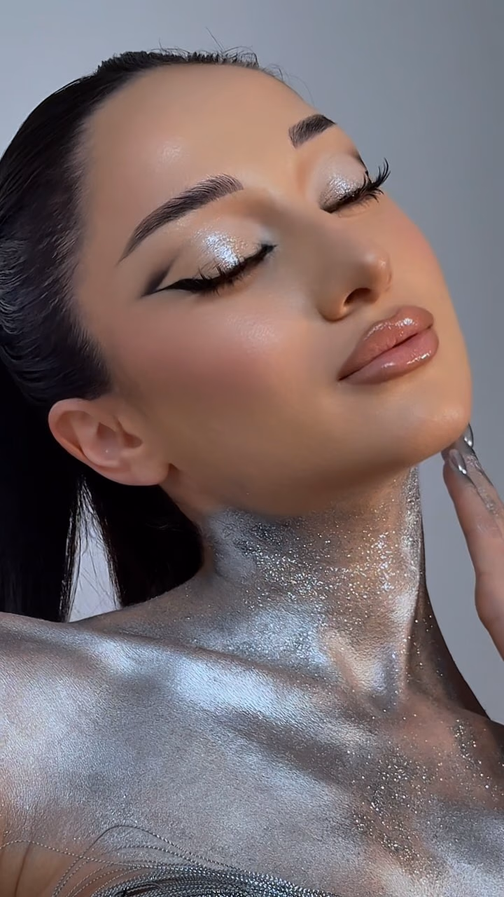 Editorial beauty look with silver metallic body shimmer, graphic black liner and a glossy lip